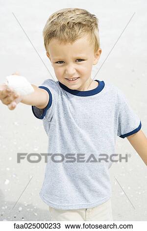 Young boy holding up seashell, smiling at camera View Large Photo Image Stock Image - Young boy holding up seashell, smiling at camera. Fotosearch