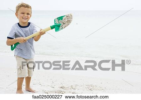 Young boy holding up shovel and throwing sand, smiling at camera View Large Photo Image Stock Photo - Young boy holding up shovel and throwing sand, smiling at camera. Fotosearch