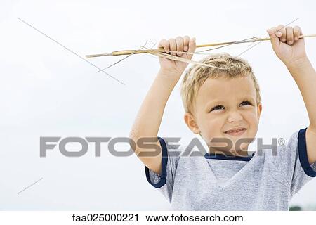 Young boy holding up stick, arms raised, smiling View Large Photo Image Stock Image - Young boy holding up stick, arms raised, smiling. Fotosearch
