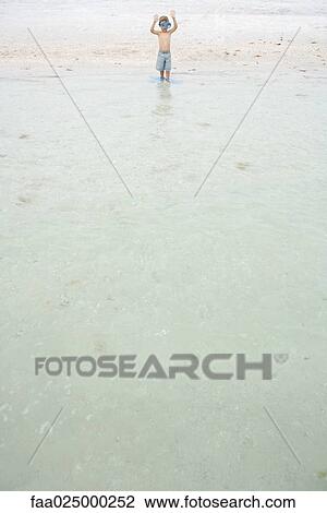 Young boy in swimming mask and flippers, standing ankle deep in water, arms raised, mid-distance View Large Photo Image Stock Image - Young boy in swimming mask and flippers, standing ankle deep in water, arms raised, mid-distance. Fotosearch
