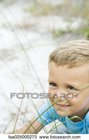 Stock Image - Young boy in tall grass, smiling, looking away, cropped view. Fotosearch