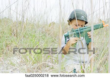 Young boy playing with toy gun, wearing helmet, looking down View Large Photo Image Stock Photo - Young boy playing with toy gun, wearing helmet, looking down. Fotosearch