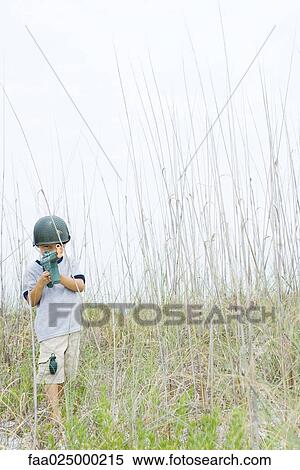 Stock Photography - Young boy pretending to be soldier, holding toy gun, looking at camera. Fotosearch