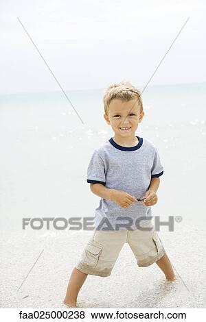 Young boy standing ankle deep in water at the beach, smiling at camera View Large Photo Image Stock Photo - Young boy standing ankle deep in water at the beach, smiling at camera. Fotosearch