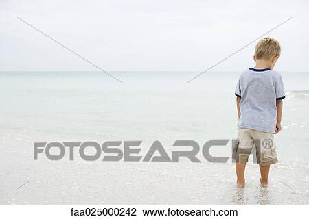 Young boy standing at the beach, looking down, rear view View Large Photo Image Stock Image - Young boy standing at the beach, looking down, rear view. Fotosearch
