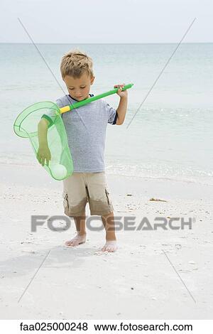 Young boy standing at the beach, reaching for ball in net View Large Photo Image Stock Photo - Young boy standing at the beach, reaching for ball in net. Fotosearch