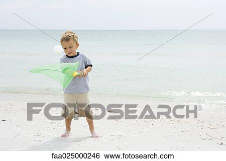 Young boy standing at the beach, trying to catch ball with net View Large Photo Image Stock Photograph - Young boy standing at the beach, trying to catch ball with net. Fotosearch
