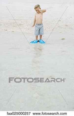 Young boy standing at the beach wearing flippers, rubbing eye, looking at camera View Large Photo Image Stock Photo - Young boy standing at the beach wearing flippers, rubbing eye, looking at camera. Fotosearch