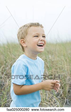 Young boy standing in tall grass, laughing, looking away View Large Photo Image Stock Image - Young boy standing in tall grass, laughing, looking away. Fotosearch