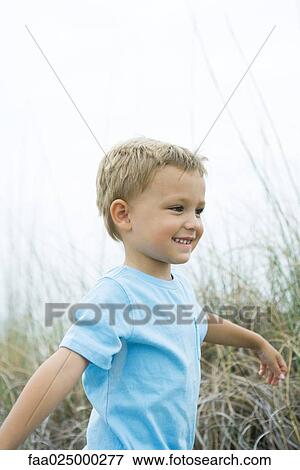 Stock Photo - Young boy standing in tall grass with arms out, looking away. Fotosearch