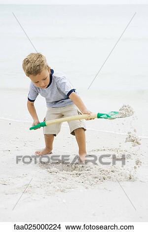 Young boy standing on beach, digging in sand with shovel, looking down View Large Photo Image Picture - Young boy standing on beach, digging in sand with shovel, looking down. Fotosearch