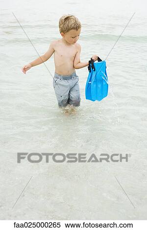 Young boy walking knee deep in water, carrying flippers, looking down View Large Photo Image Stock Photography - Young boy walking knee deep in water, carrying flippers, looking down. Fotosearch