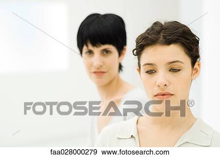Young businesswoman looking down, colleague standing behind her, looking at camera View Large Photo Image Stock Photo - Young businesswoman looking down, colleague standing behind her, looking at camera. Fotosearch