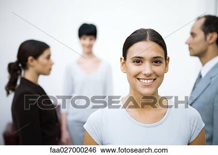 Young businesswoman smiling at camera, colleagues standing in background View Large Photo Image Stock Photograph - Young businesswoman smiling at camera, colleagues standing in background. Fotosearch