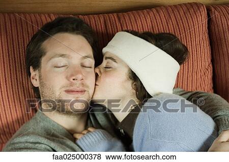 Young couple reclining on couch, woman kissing man on cheek, eyes closed View Large Photo Image Stock Photo - Young couple reclining on couch, woman kissing man on cheek, eyes closed. Fotosearch
