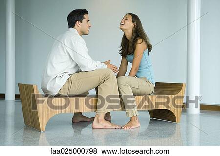 Young couple sitting face to face on bench, laughing together View Large Photo Image Stock Photo - Young couple sitting face to face on bench, laughing together. Fotosearch