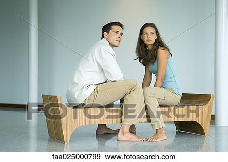 Stock Photo - Young couple sitting face to face on bench, both looking away. Fotosearch