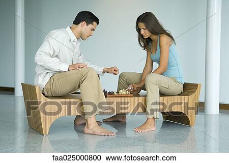 Young couple sitting on bench, looking down at chess board together View Large Photo Image Stock Image - Young couple sitting on bench, looking down at chess board together. Fotosearch