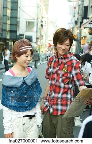 Stock Image - Young couple standing on city street, looking at package together. Fotosearch
