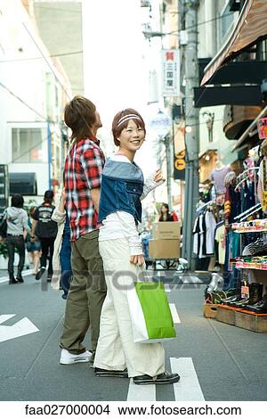 Young couple walking in street, woman carrying shopping bag, smiling over shoulder at camera View Large Photo Image Picture - Young couple walking in street, woman carrying shopping bag, smiling over shoulder at camera. Fotosearch