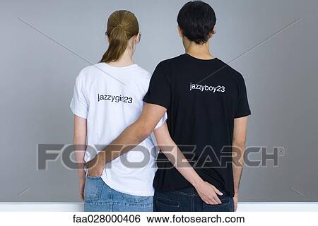 Young couple wearing customized tee-shirts, arms around each other's waists, rear view View Large Photo Image Stock Photograph - Young couple wearing customized tee-shirts, arms around each other's waists, rear view. Fotosearch