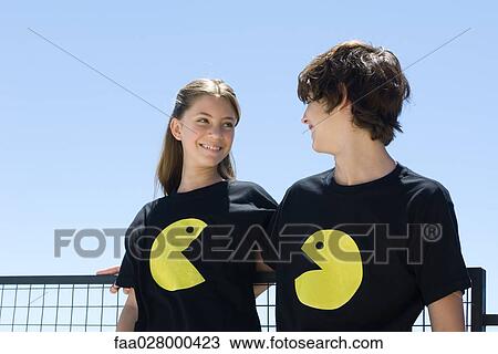 Young couple wearing tee-shirts printed with graphic characters, smiling at each other View Large Photo Image Stock Image - Young couple wearing tee-shirts printed with graphic characters, smiling at each other. Fotosearch