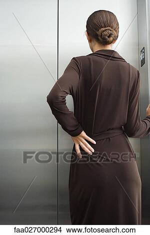 Young female standing in front of elevator, hand on hip, rear view View Large Photo Image Picture - Young female standing in front of elevator, hand on hip, rear view. Fotosearch