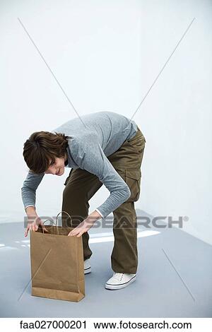 Young man bending over paper shopping bag, looking away, smiling View Large Photo Image Stock Image - Young man bending over paper shopping bag, looking away, smiling. Fotosearch