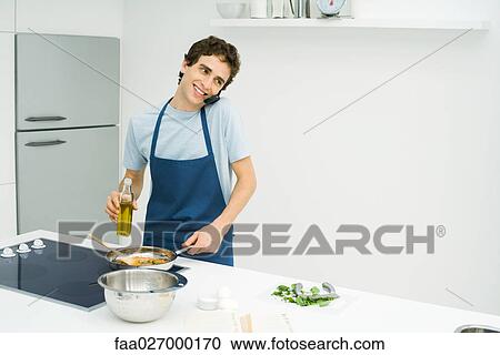 Young man cooking at stove, using cell phone, smiling View Large Photo Image Stock Image - Young man cooking at stove, using cell phone, smiling. Fotosearch
