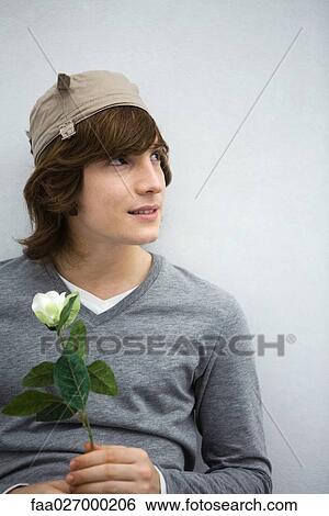 Young man holding flower, looking away, smiling, close-up View Large Photo Image Stock Photograph - Young man holding flower, looking away, smiling, close-up. Fotosearch