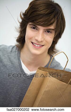 Young man holding shopping bag, smiling at camera, portrait View Large Photo Image Stock Image - Young man holding shopping bag, smiling at camera, portrait. Fotosearch