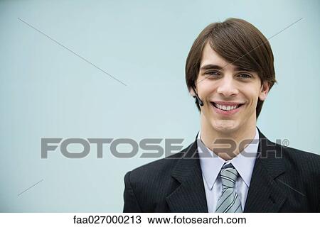 Stock Image - Young man in suit using headset, smiling at camera, portrait. Fotosearch