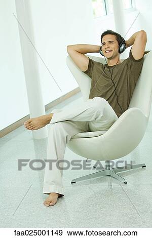 Young man listening to headphones with hands behind head, smiling, full length View Large Photo Image Stock Photo - Young man listening to headphones with hands behind head, smiling, full length. Fotosearch
