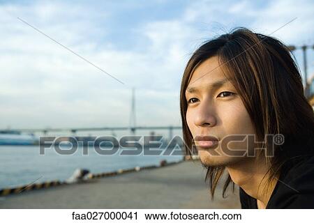 Young man looking away, waterfront in background View Large Photo Image Stock Image - Young man looking away, waterfront in background. Fotosearch