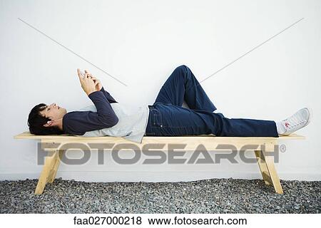 Young man lying on bench, listening to mp3 player, side view View Large Photo Image Stock Photo - Young man lying on bench, listening to mp3 player, side view. Fotosearch