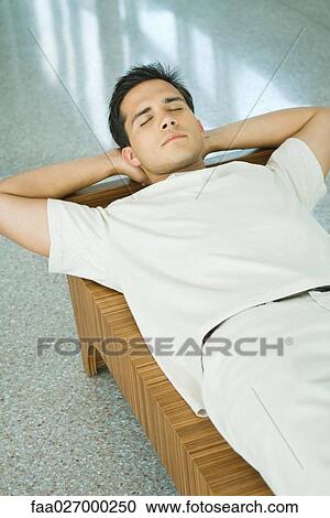 Young man lying on bench with hands behind head, eyes closed View Large Photo Image Stock Image - Young man lying on bench with hands behind head, eyes closed. Fotosearch