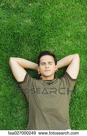Young man lying on grass with hands behind head, eyes closed, high angle view View Large Photo Image Stock Photo - Young man lying on grass with hands behind head, eyes closed, high angle view. Fotosearch