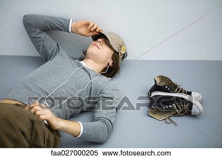Young man lying on the ground with eyes closed, listening to earphones View Large Photo Image Stock Photography - Young man lying on the ground with eyes closed, listening to earphones. Fotosearch