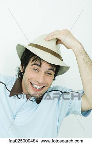 Young man putting hat on head, smiling at camera View Large Photo Image Picture - Young man putting hat on head, smiling at camera. Fotosearch