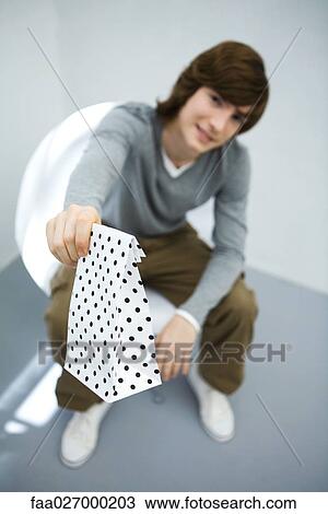 Young man sitting in chair, holding gift bag toward camera, focus on foreground View Large Photo Image Stock Image - Young man sitting in chair, holding gift bag toward camera, focus on foreground. Fotosearch