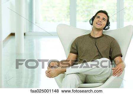 Young man sitting in chair listening to headphones, smiling View Large Photo Image Stock Photo - Young man sitting in chair listening to headphones, smiling. Fotosearch