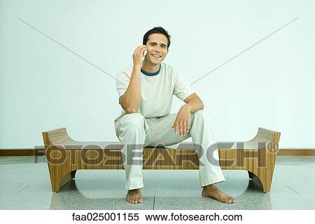 Young man sitting on bench using cell phone View Large Photo Image Stock Photography - Young man sitting on bench using cell phone. Fotosearch