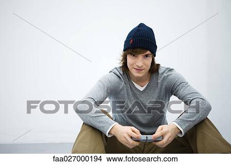 Young man sitting on the ground, holding video game controller, smiling at camera View Large Photo Image Picture - Young man sitting on the ground, holding video game controller, smiling at camera. Fotosearch