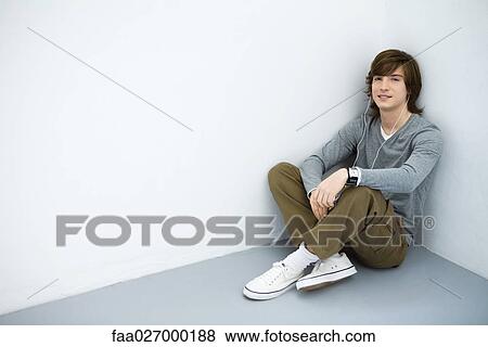 Young man sitting on the ground, listening to mp3 player, smiling at camera View Large Photo Image Stock Photo - Young man sitting on the ground, listening to mp3 player, smiling at camera. Fotosearch