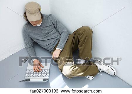 Young man sitting on the ground, using laptop computer, high angle view View Large Photo Image Stock Image - Young man sitting on the ground, using laptop computer, high angle view. Fotosearch