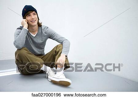 Young man sitting on the ground, using cell phone, smiling View Large Photo Image Stock Photograph - Young man sitting on the ground, using cell phone, smiling. Fotosearch