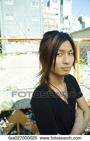 Young man standing outdoors with arms folded, looking away View Large Photo Image Stock Photography - Young man standing outdoors with arms folded, looking away. Fotosearch