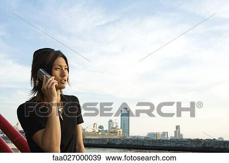 Young man using cell phone outdoors, looking away, cityscape in background View Large Photo Image Stock Photo - Young man using cell phone outdoors, looking away, cityscape in background. Fotosearch