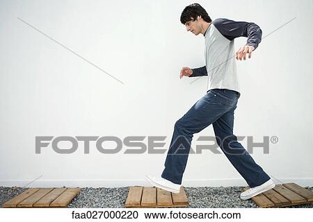 Young man walking on path, listening to earphones, side view View Large Photo Image Stock Image - Young man walking on path, listening to earphones, side view. Fotosearch