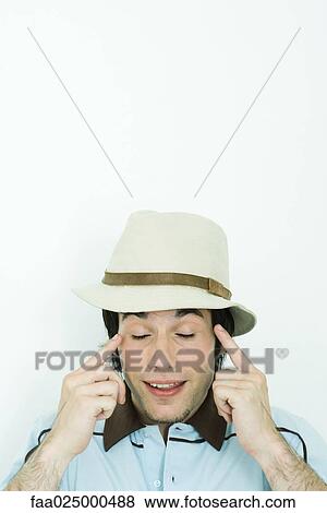 Young man wearing hat, pointing at temples, eyes closed View Large Photo Image Stock Photo - Young man wearing hat, pointing at temples, eyes closed. Fotosearch